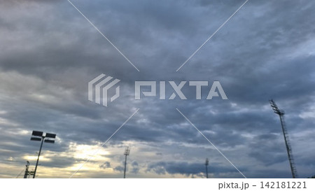 Slightly blurry shot captures warm sunset light breaking through clouds behind stadium floodlight towers Slightly blurry shot captures warm sunset light breaking through clouds behind stadium floodlight towers 142181221