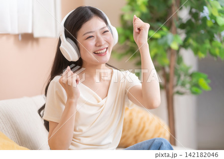 ヘッドフォンをつけて音楽を聴きながら笑顔で盛り上がる若い女性 ヘッドフォンをつけて音楽を聴きながら笑顔で盛り上がる若い女性 142182046