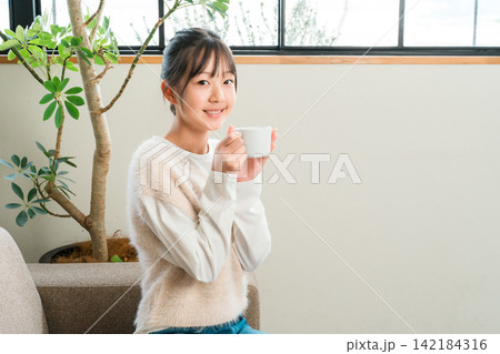 自宅のリビングでホットドリンクを飲む小学生,中学生の女の子 自宅のリビングでホットドリンクを飲む小学生,中学生の女の子 142184316