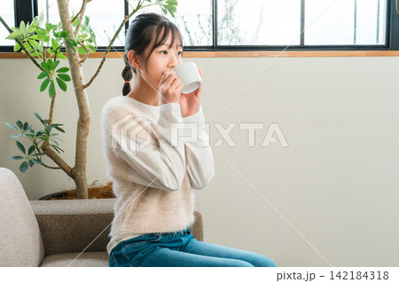 自宅のリビングでホットドリンクを飲む小学生,中学生の女の子 自宅のリビングでホットドリンクを飲む小学生,中学生の女の子 142184318