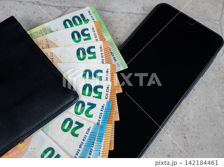 Paper money in black partmone and smartphone on the table. Cash euro bills in leather wallet with mobile phone for commerce concept. Paper money in black partmone and smartphone on the table. Cash euro bills in leather wallet with mobile phone for commerce concept. 142184461