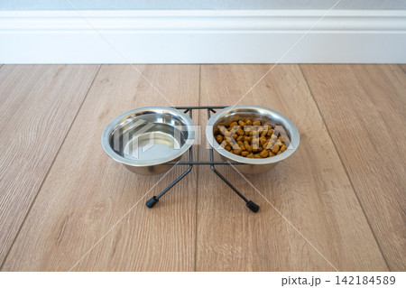 A bowl with dry dog kibble food and water on the wood floor. Snack for dogs. A bowl with dry dog kibble food and water on the wood floor. Snack for dogs. 142184589