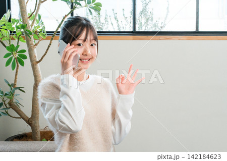 自宅のソファに座りスマホで通話する小学生,中学生の女の子 142184623