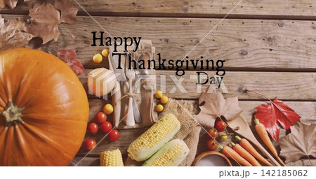 Orange pumpkin sitting left on rustic plank with cutlery, Happy Thanksgiving Day text, copy space 142185062