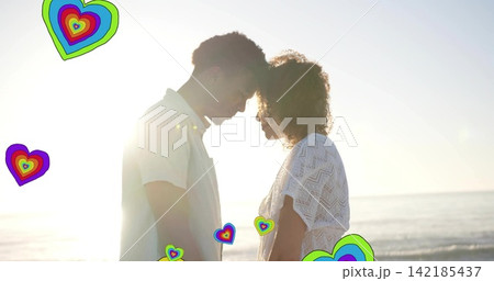 Standing couple touching foreheads at beach, wearing lace dress and light shirt, hearts, sun flare. Silhouette, romance, backlit, sunset, coastline, intimacy, colorful 142185437
