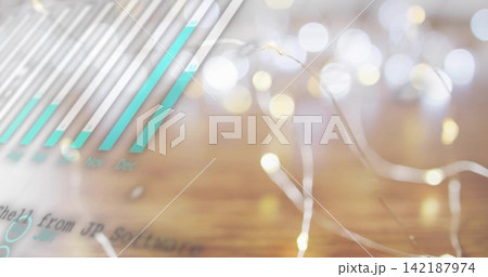 Glowing thin-wire fairy lights resting on warm wooden tabletop, showing teal bar chart overlay 142187974