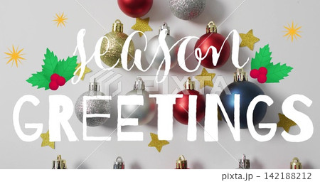 Showing festive flatlay on white surface with metal baubles, holly, gold stars, season GREETINGS Showing festive flatlay on white surface with metal baubles, holly, gold stars, season GREETINGS 142188212