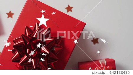 Displaying large red gift box with glossy metallic star bow on pale grey tabletop, gold confetti 142188450