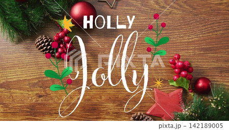 Showing white handlettered Jolly and HOLLY text sitting on wood, with pine sprig, berries, bauble Showing white handlettered Jolly and HOLLY text sitting on wood, with pine sprig, berries, bauble 142189005