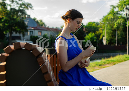Girl with book under summer trees. Digital detox moment. Brain refreshes with each page. Harmony with surrounding greenery. Simple seasonal joy of outdoor reading Girl with book under summer trees. Digital detox moment. Brain refreshes with each page. Harmony with surrounding greenery. Simple seasonal joy of outdoor reading 142191525