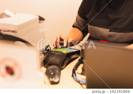 Woman cashier using a touchscreen credit card payment terminal at store counter. 142191869