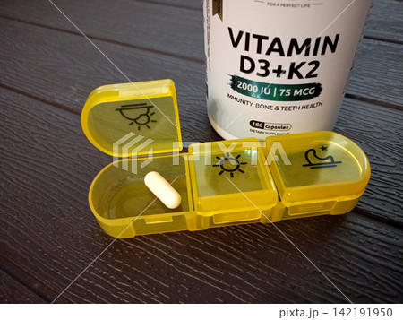 On the table is a medication organizer with vitamin D capsule in front and a jar On the table is a medication organizer with vitamin D capsule in front and a jar 142191950