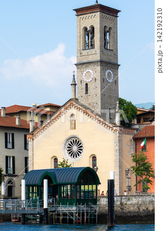 Ancient Church of Saint Thecla in Torno Facade with Clock Tower on a Lake Shore behind a Ferry Pier Como Italy Ancient Church of Saint Thecla in Torno Facade with Clock Tower on a Lake Shore behind a Ferry Pier Como Italy 142192310