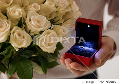Man holding red velvet jewelry box with diamond ring and bouquet of white roses for marriage proposal Man holding red velvet jewelry box with diamond ring and bouquet of white roses for marriage proposal 142193903