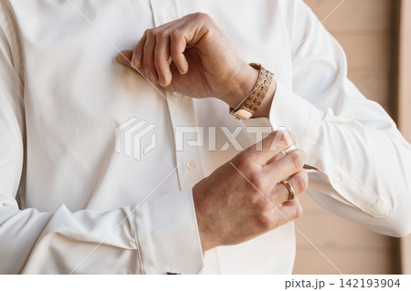 Close up of man adjusting cuff of white formal dress shirt wearing gold watch and wedding ring. Close up of man adjusting cuff of white formal dress shirt wearing gold watch and wedding ring. 142193904