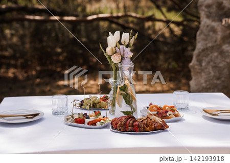 Elegant outdoor breakfast table with croissants, fresh fruit, and white tulips on a white linen tablecloth. 142193918
