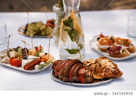 Gourmet Brunch Spread with Croissants Appetizers and Infused Water on White Tablecloth Outdoors 142193919
