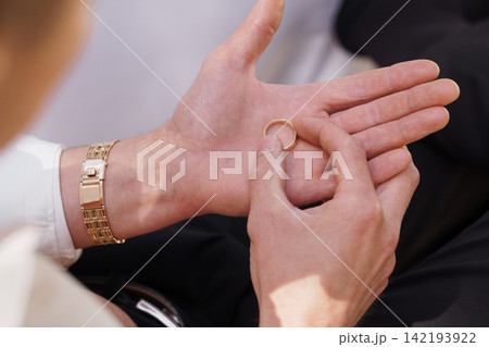 Close up of man holding a gold wedding band in open palm wearing a gold watch and black trousers. 142193922