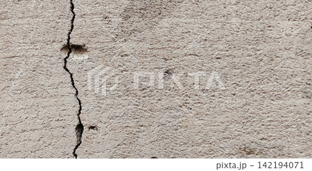 Vertical cracks in the rough texture of a cement wall. 142194071