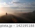 朝靄の堤防を歩いていく一人の人影 142195188