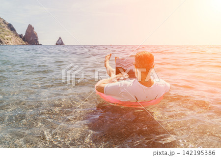 Freelance beach laptop man works while floating on inflatable ring in the sea during a tropical summer vacation under bright sunlight Freelance beach laptop man works while floating on inflatable ring in the sea during a tropical summer vacation under bright sunlight 142195386