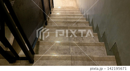 Modern tiled staircase with a black metal mesh railing. Modern tiled staircase with a black metal mesh railing. 142195671