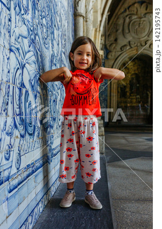 Young Smiling Girl Standing next to Traditional Blue Azulejo Tiles in Porto, Portugal looking at camera 142195743