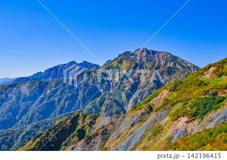 秋の快晴の朝 唐松岳の登山道から色付いた山肌越しに望む雲が浮かぶ遠方の山並み 142196415