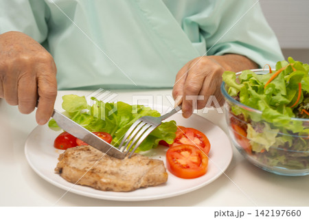 Asian elderly woman patient eating pork chop stake and vegetable salad for healthy food in hospital. Asian elderly woman patient eating pork chop stake and vegetable salad for healthy food in hospital. 142197660