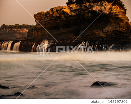 Long exposure view of silky sea water moving over dark rock terraces below rocky cliffs at Klayar Beach (Pantai Klayar), Pacitan, East Java, Indonesia. 142197801