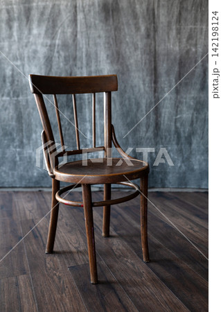 Vintage wooden chair on dark hardwood floor against textured grey canvas backdrop in minimalist photo studio space. Vintage wooden chair on dark hardwood floor against textured grey canvas backdrop in minimalist photo studio space. 142198124