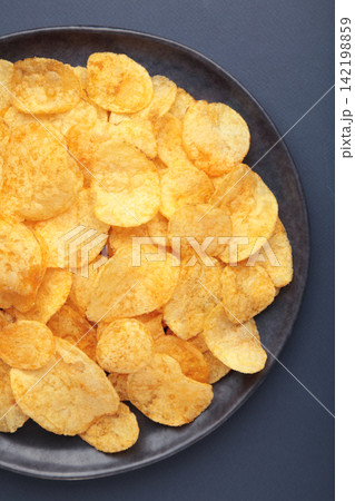 Potato chips on dark plate on dark blue background. Potato chips on dark plate on dark blue background. 142198859