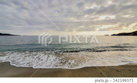Sea waves foam washing sandy beach shoreline under cloudy sky during sunset in Greece Mediterranean coast stock photo Sea waves foam washing sandy beach shoreline under cloudy sky during sunset in Greece Mediterranean coast stock photo 142199371