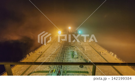 Night view from navigation bridge deck over illuminated oil tanker bow surrounded by dense fog and poor visibility at sea stock photo 142199384