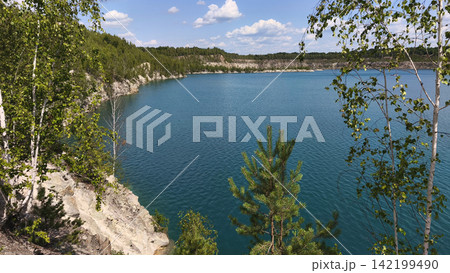 Scenic blue quarry lake surrounded by birch and pine trees, rocky cliffs and lush forest under a bright summer sky, creating a peaceful natural landscape for travel and outdoor concepts. Scenic blue quarry lake surrounded by birch and pine trees, rocky cliffs and lush forest under a bright summer sky, creating a peaceful natural landscape for travel and outdoor concepts. 142199490