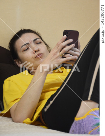 A young, beautiful woman is lying on the sofa with a phone in her hands A young, beautiful woman is lying on the sofa with a phone in her hands 142200771