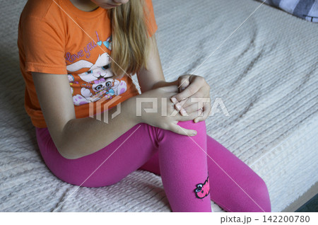 A beautiful young woman in casual clothing is holding her knee. A beautiful young woman in casual clothing is holding her knee. 142200780