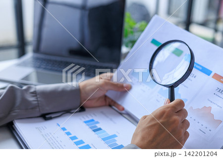 Closeup Businessman Analyzing or Auditing Financial Growth Charts with Magnifying Glass in the office. 142201204