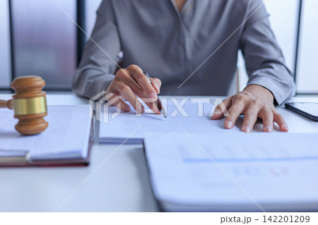 Professional lawyer working at desk reviewing legal documents next to a wooden gavel in the office. Professional lawyer working at desk reviewing legal documents next to a wooden gavel in the office. 142201209