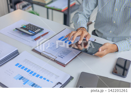 Businessman working in office using tablet while reviewing and analyzing graph data at desk. Businessman working in office using tablet while reviewing and analyzing graph data at desk. 142201261
