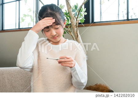 自宅のソファに座り体調不良で体温計で検温する小学生,中学生の女の子 自宅のソファに座り体調不良で体温計で検温する小学生,中学生の女の子 142202010