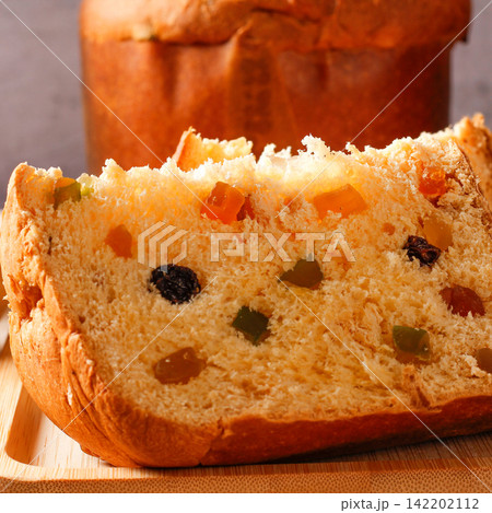 A slice of traditional Christmas panettone, showing its soft, fluffy crumb, candied fruit, and raisins, on a bamboo tray 142202112
