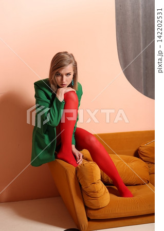 Lady in green blazer posing on colorful mustard sofa in studio setting Lady in green blazer posing on colorful mustard sofa in studio setting 142202531