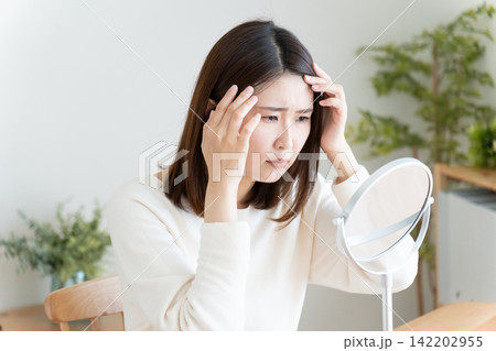 髪の毛の生え際を鏡でチェックする女性 髪の毛の生え際を鏡でチェックする女性 142202955