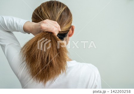 Rear view of young Asian woman holding her damaged hair like a ponytail hairstyle. It may also look dull or frizzy and be difficult to manage. Rear view of young Asian woman holding her damaged hair like a ponytail hairstyle. It may also look dull or frizzy and be difficult to manage. 142203258