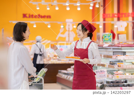 スーパーマーケットで女性客に試飲ドリンクを勧める笑顔の女性スタッフ スーパーマーケットで女性客に試飲ドリンクを勧める笑顔の女性スタッフ 142203297