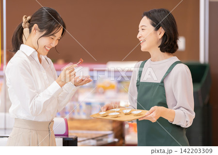 スーパーマーケットで女性客に試食を提供する笑顔の女性スタッフ スーパーマーケットで女性客に試食を提供する笑顔の女性スタッフ 142203309