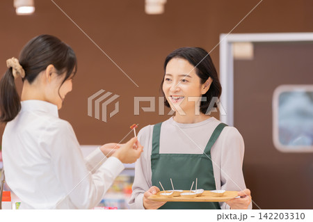 スーパーマーケットで女性客に試食を提供する笑顔の女性スタッフ スーパーマーケットで女性客に試食を提供する笑顔の女性スタッフ 142203310
