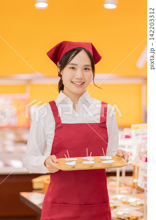 スーパーマーケットで試食をおすすめする笑顔の女性スタッフ スーパーマーケットで試食をおすすめする笑顔の女性スタッフ 142203312