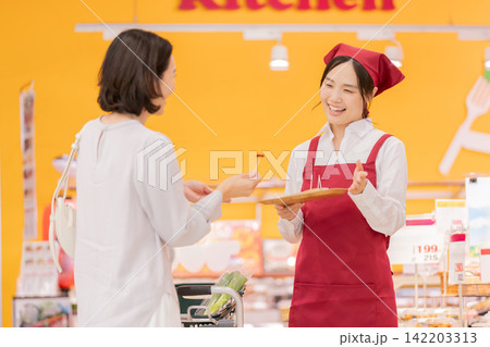 スーパーマーケットで女性客に試食を勧める笑顔の女性スタッフ スーパーマーケットで女性客に試食を勧める笑顔の女性スタッフ 142203313